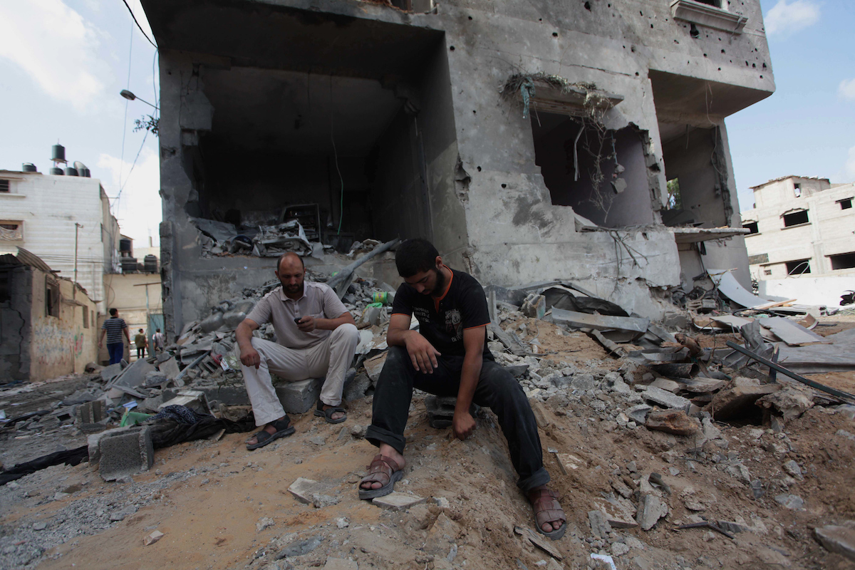 Palestinian men sit amidst the debris of a neighbouring house which police said was damaged after an Israeli air strike destroyed Tayseer Al-Batsh's family house, in Gaza City July 13, 2014. (Photo: Ashraf Amra/APA Images)